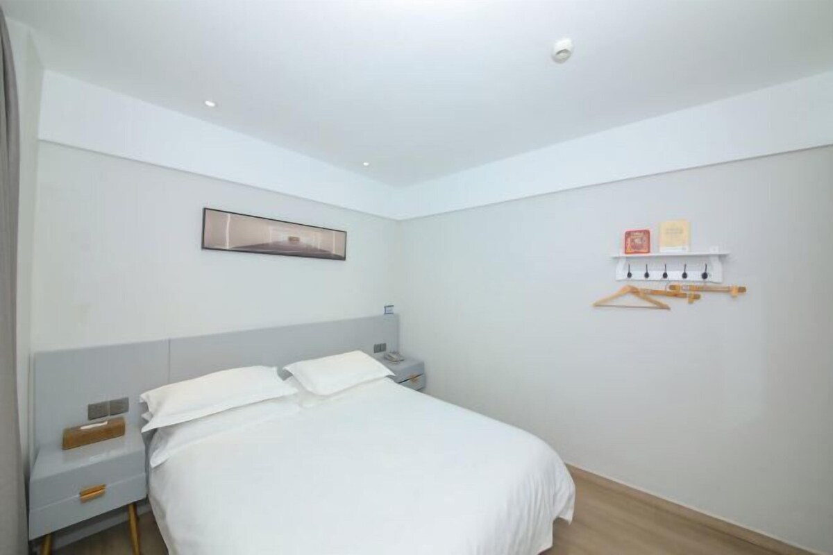 Une chambre à coucher comprenant un lit, une table de chevet, une commode, une étagère fixée au mur et un tableau encadré.