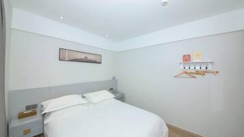 Un dormitorio con cama, mesita de noche, repisa y estante en la pared, además de un cuadro enmarcado.