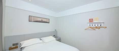 A bedroom with a bed, bedside table, nightstand, wall-mounted shelf, and a framed picture.