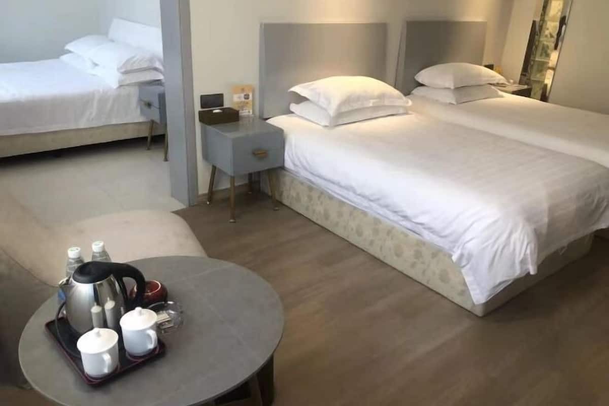 Ein Hotelzimmer mit einem Bett, einem Nachttisch mit Lampe, einem kleinen Tisch mit Wasserkocher und Tassen sowie einem Sessel.