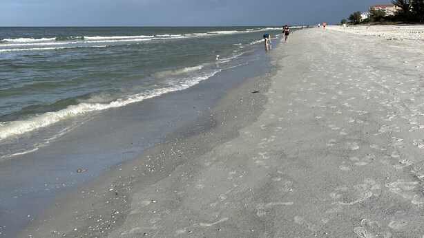 A beach with a wide sandy shore, a few people walking, and a building in the background.