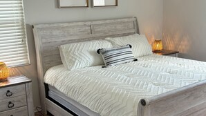 A bedroom with a wooden bed, two bedside tables with lamps, a gray rug, and two framed pictures on the wall.