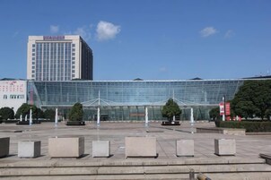 Un edificio moderno con fachada de vidrio, un amplio vestíbulo con escalones y algunos árboles.