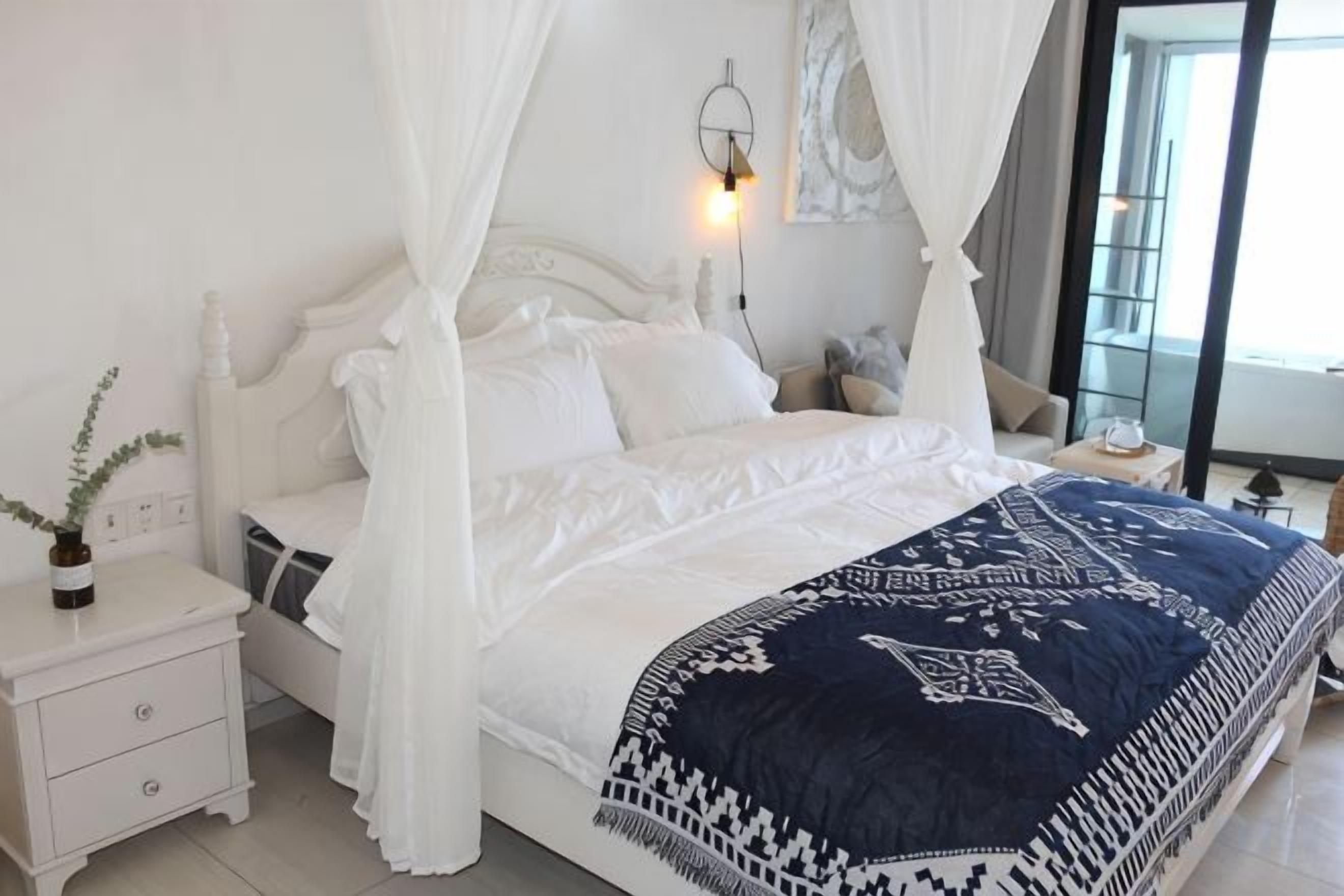 A bed with a canopy, bedside table, and a lamp.