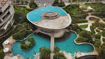 A large circular pool with a central fountain, surrounded by lush greenery and multiple smaller pools.