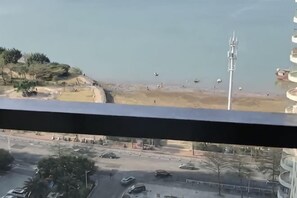 Uitzicht vanaf een balkon op een strand, met daaronder een weg en geparkeerde auto's.