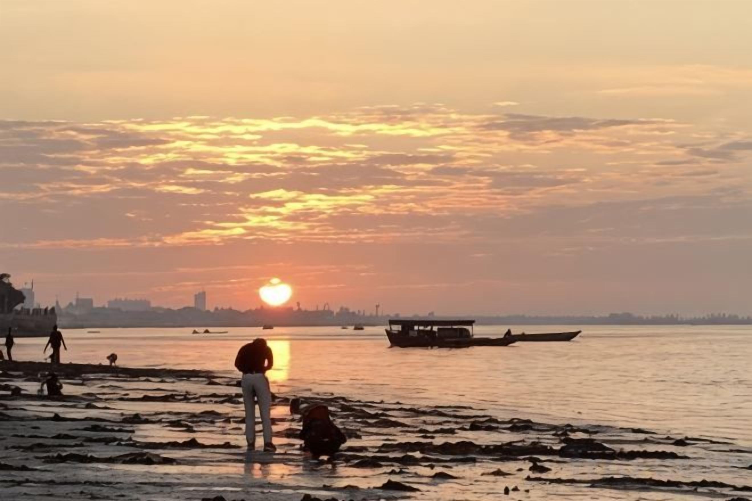 A sunset over a body of water with a boat and people on the shore.