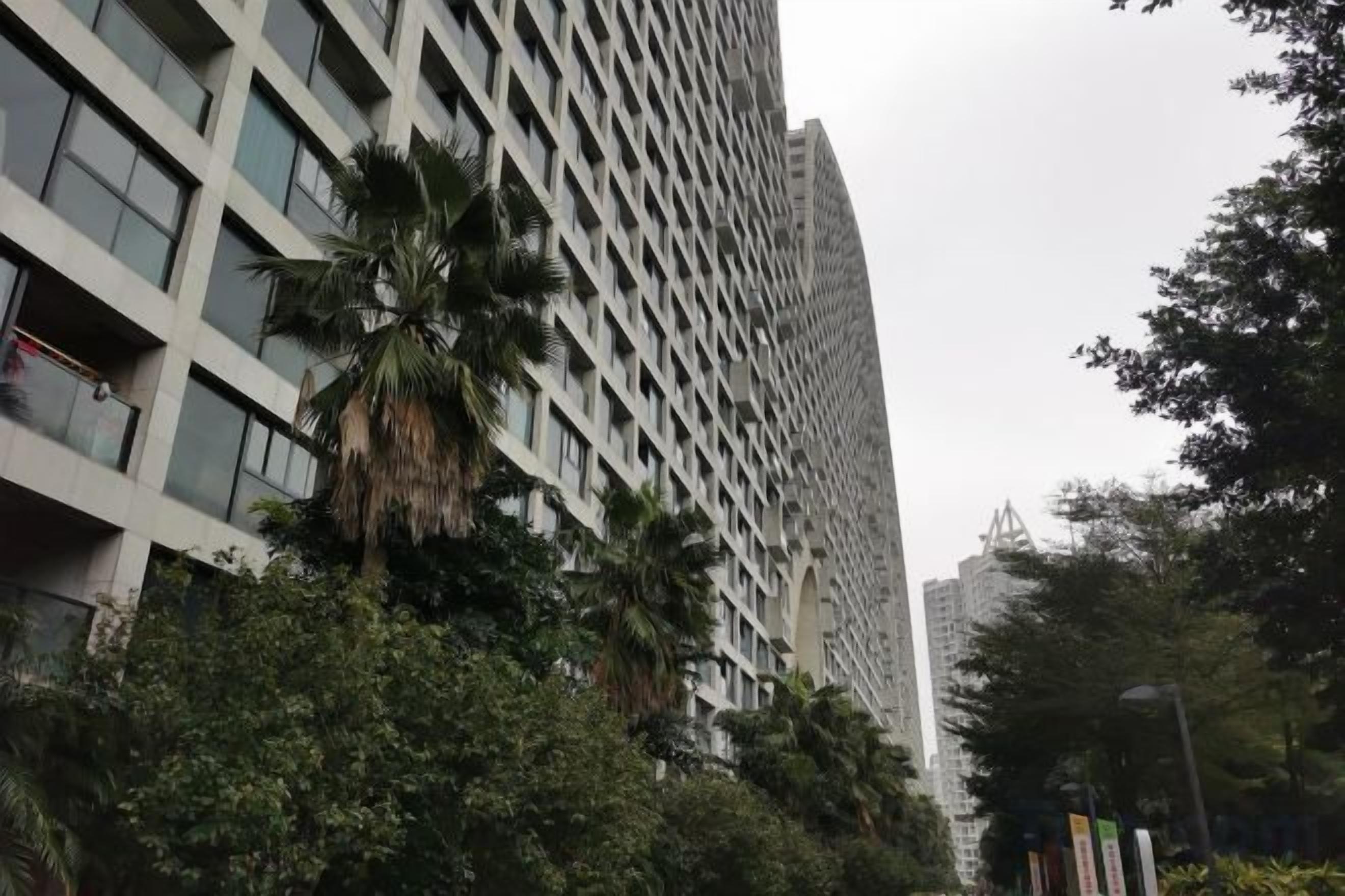 A tall building with a grid-like facade, surrounded by trees and greenery.