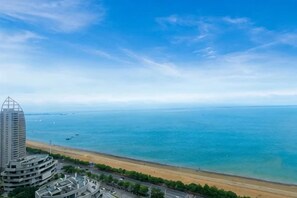 A coastal view with a beach, ocean, and a tall building with a unique architectural design. - Aizhihai (Beihai)