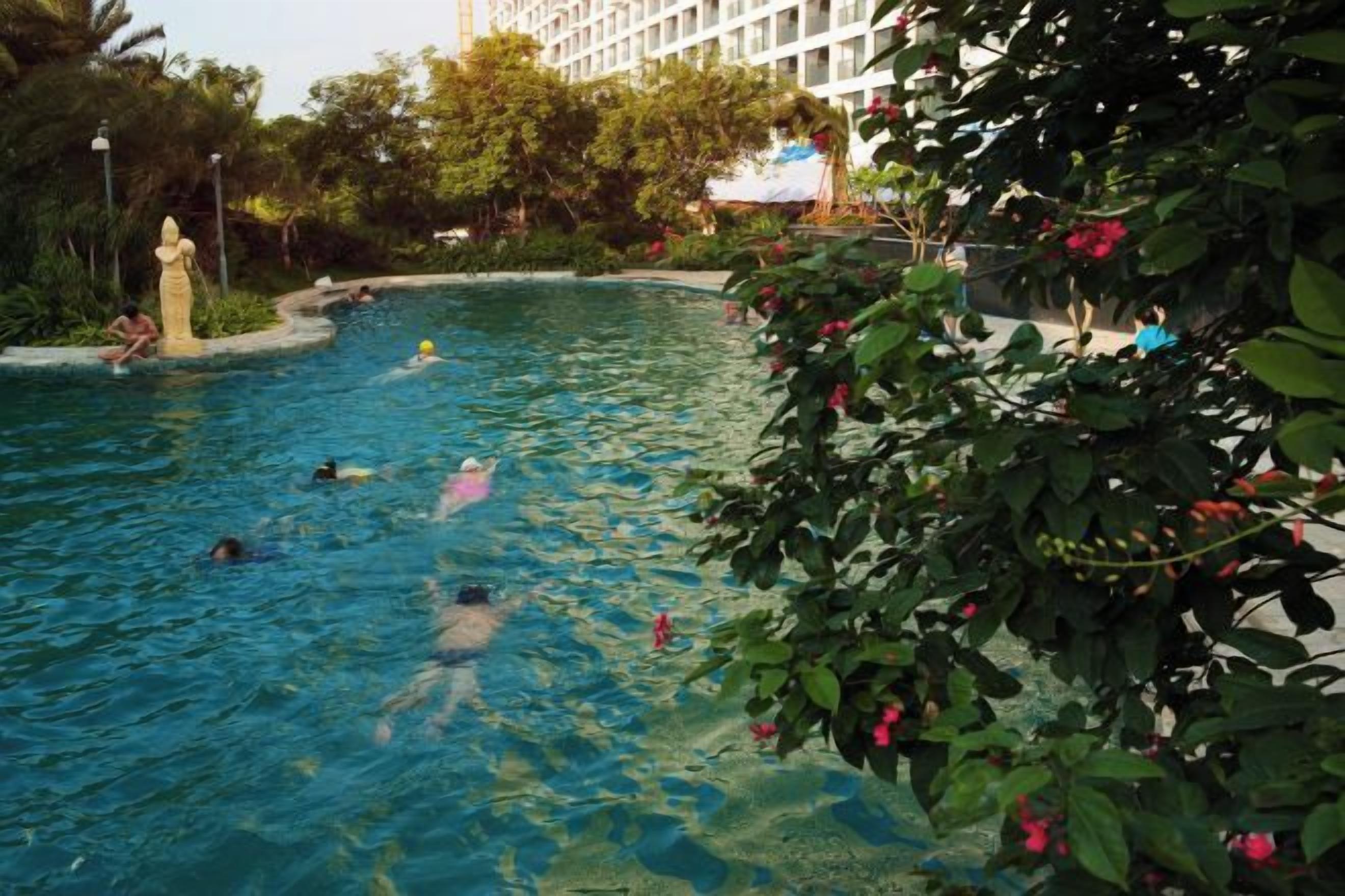 A swimming pool surrounded by lush greenery and a building in the background.