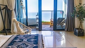 A room with a bed, a hanging chair, a balcony with a table and chairs, and a view of the sea. - Aizhihai (Beihai)