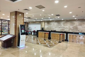 Zona de recepción de un hotel con quiosco digital, mostrador de registro y fila de espera.