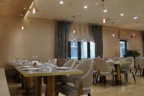 A dining area with tables and chairs, a large window with curtains, and hanging lights. - Xiyu International Hotel (Urumqi)