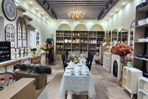 Interior bem iluminado com mesa de jantar posta para refeição, cercada por prateleiras com objetos decorativos e móveis.