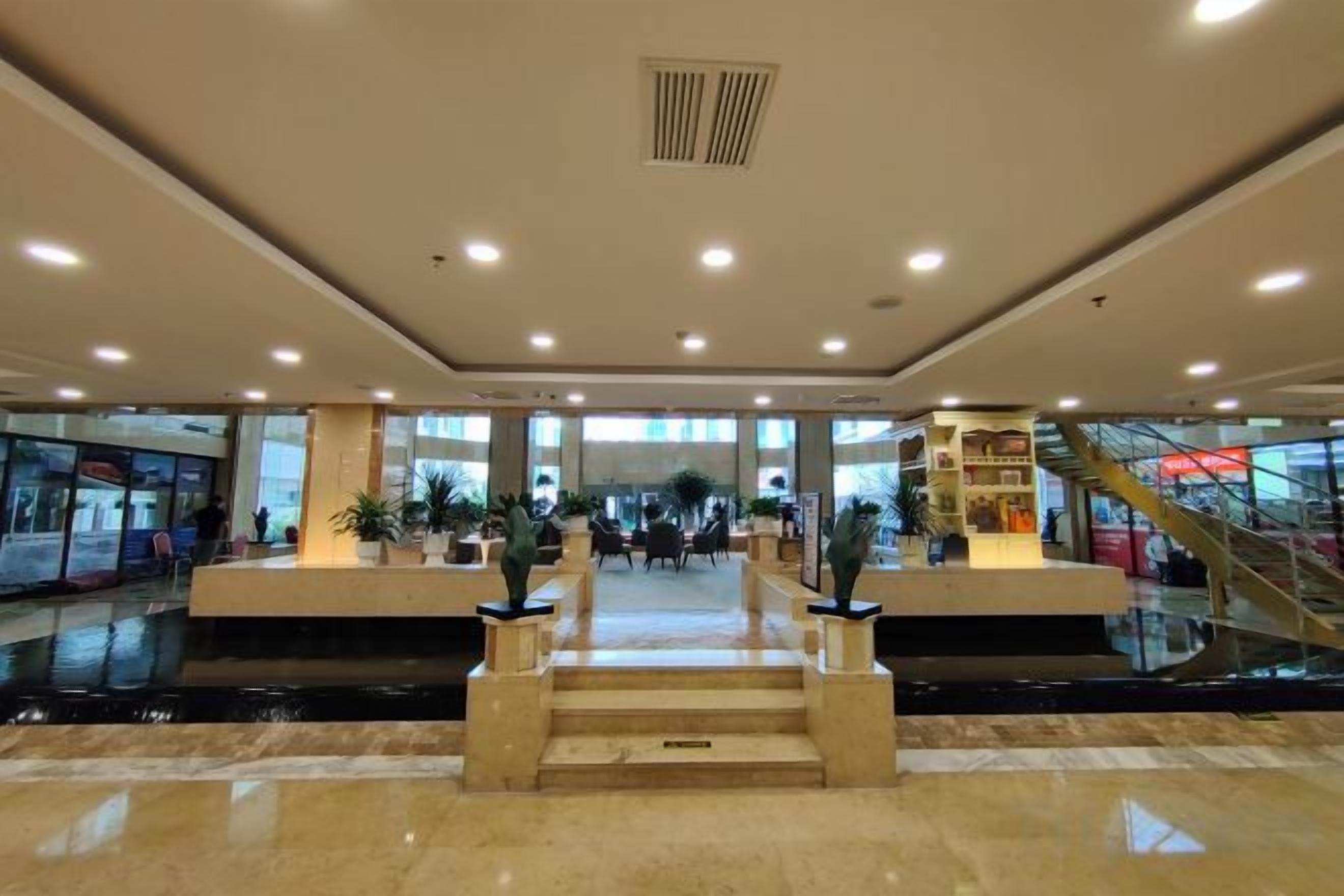 A spacious indoor area with a central staircase, a water feature, and a glass facade in the background.