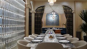 Zona pranzo con un tavolo lungo apparecchiato per un pasto, circondato da sedie, una parete decorativa e un lampadario.