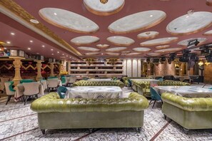 Un hall de hotel con sofás tapizados en verde, suelo con diseño de mármol y techo con motivos circulares.