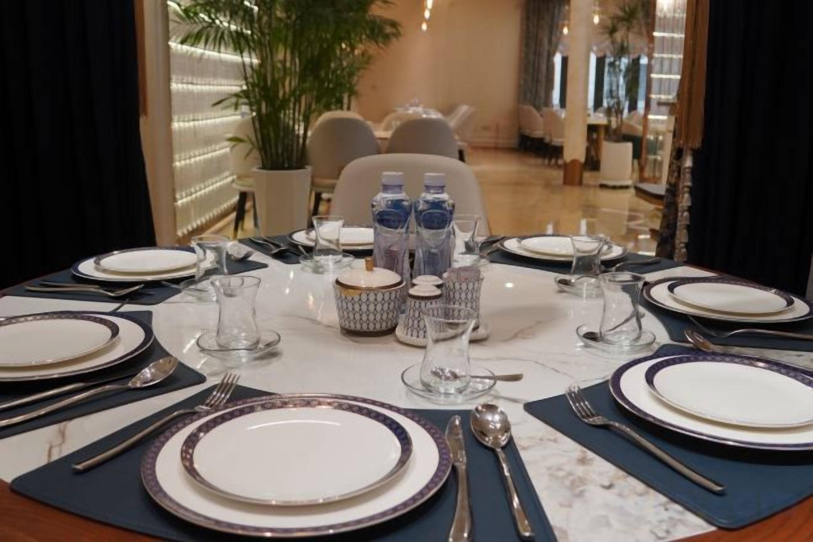 A dining table set for four with plates, cutlery, glasses, and water bottles.
