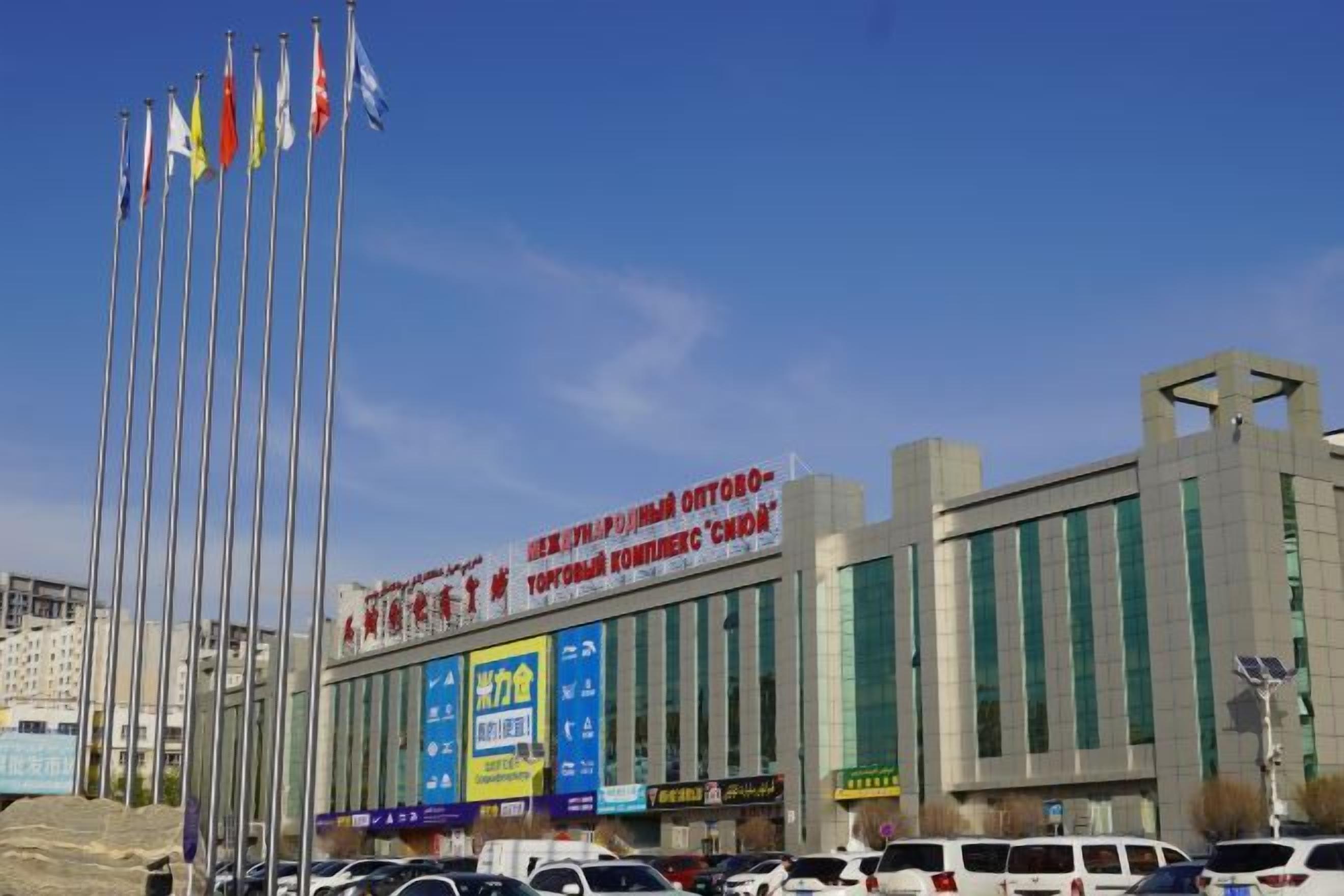 A building with multiple flags, a large sign, and several cars parked in front.