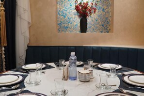 Une table à manger est dressée avec des assiettes, des verres et des couverts, et un vase rempli de fleurs rouges est posé sur le mur derrière.