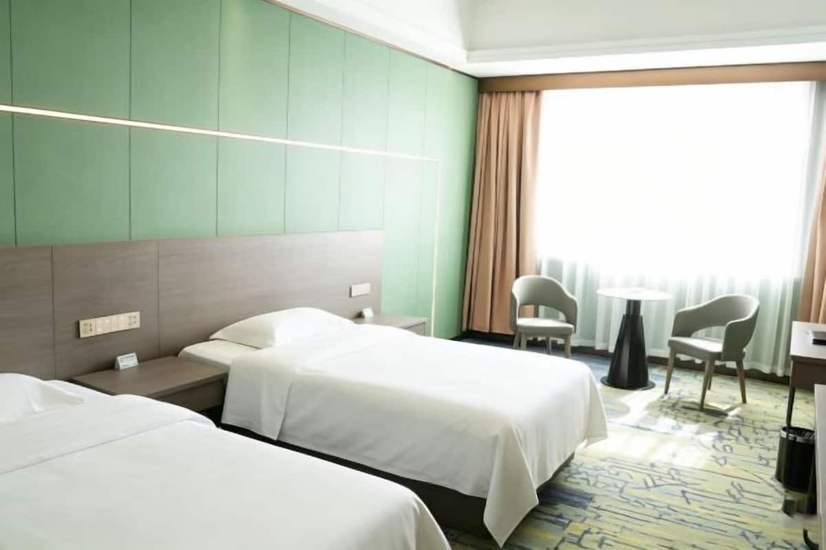 A hotel room with two beds, a desk, chairs, and a large window with curtains.
