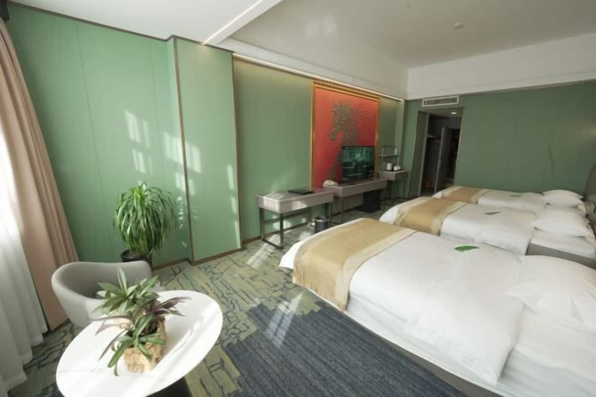 A hotel room with a bed, a desk, a chair, and a potted plant.