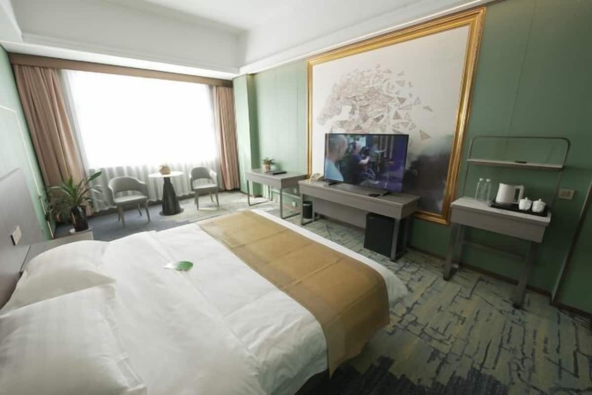 A hotel room with a large bed, a desk with a television, a small table, and a chair.