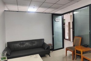 Quarto com sofá de couro preto, mesa redonda pequena e uma cadeira.