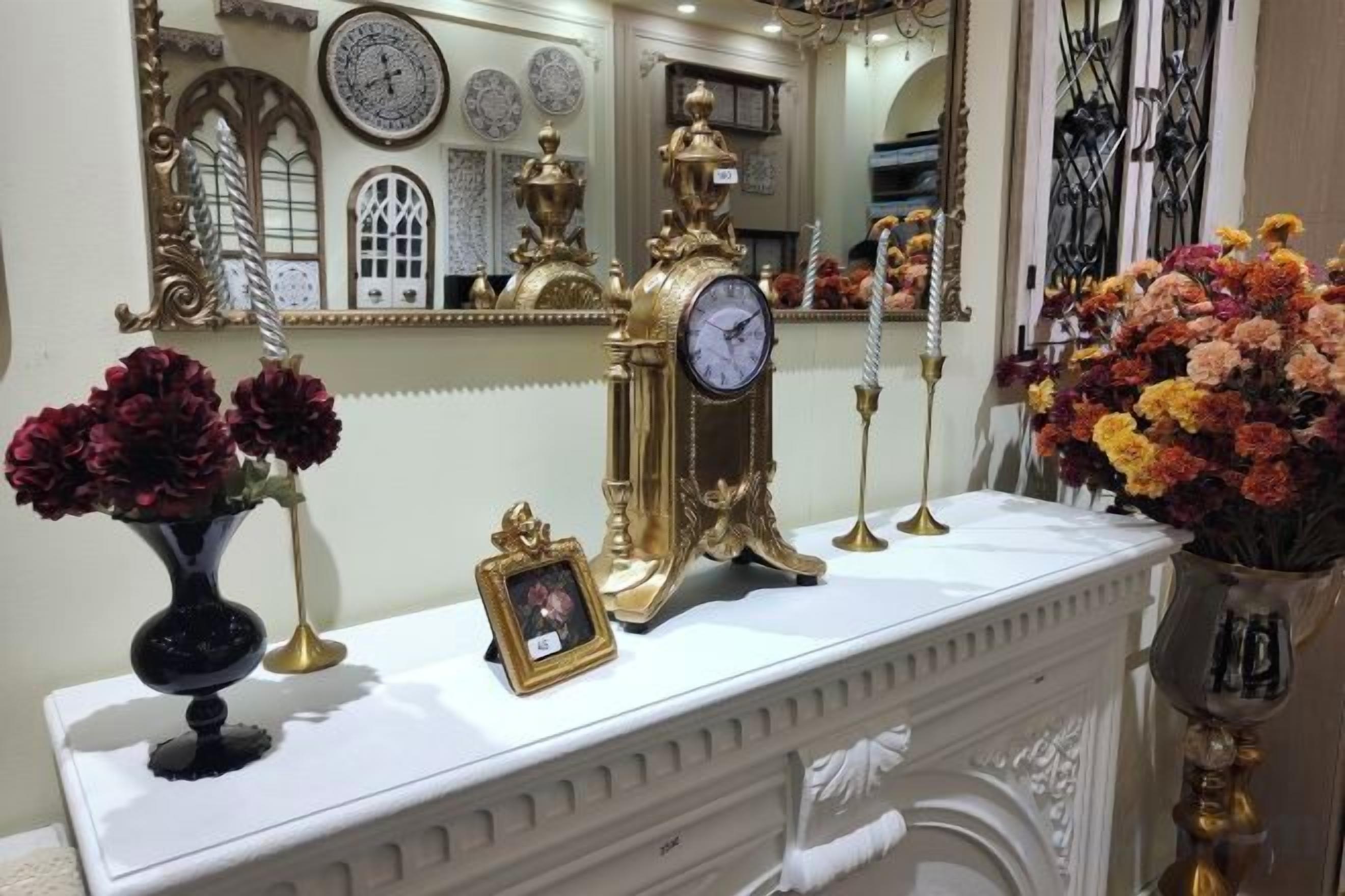 A white mantelpiece with a clock, vases with flowers, and a framed picture.