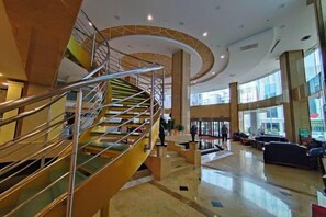 Eine geräumige Lobby mit einer zentralen Treppe, einem Empfangsbereich und einer Sitzecke.