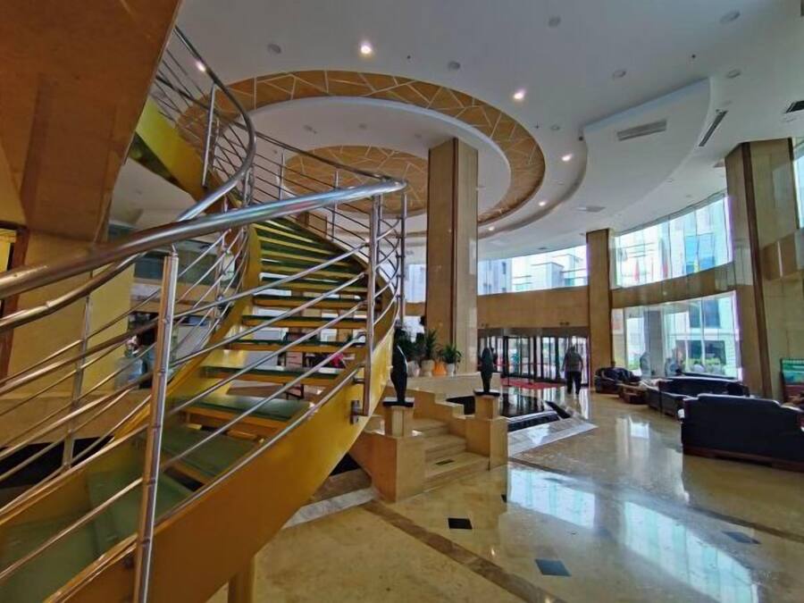 Um hall espaçoso com uma escadaria central, áreas de estar e grandes janelas que permitem a entrada de luz natural.