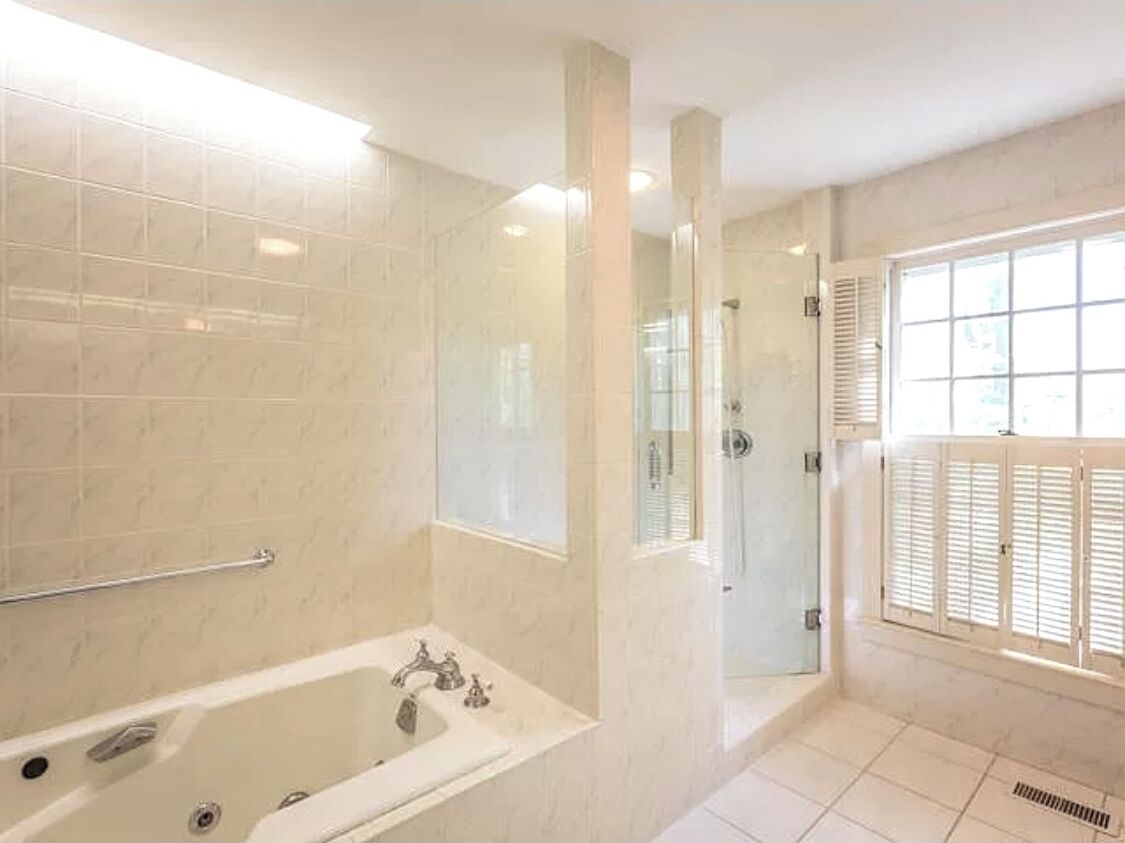 Un baño con bañera, ducha y ventana con persianas.