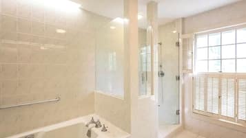 Un baño con bañera, ducha y ventana con persianas.