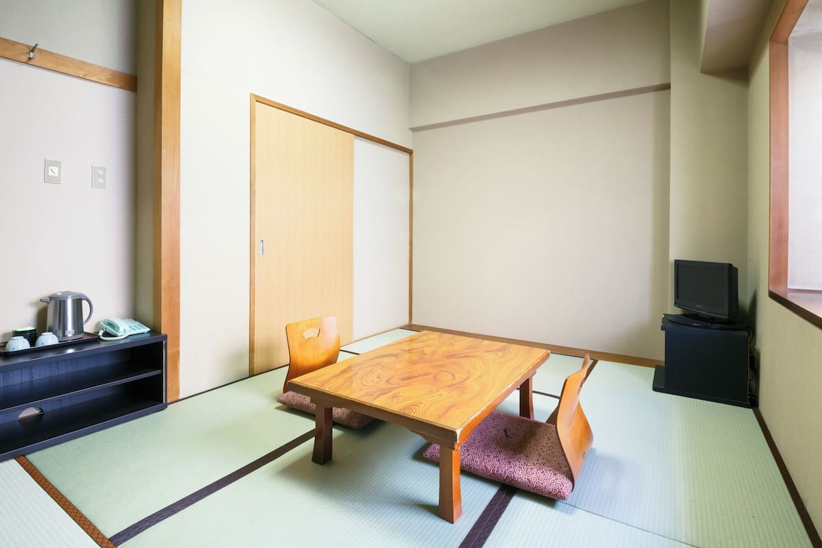 A traditional Japanese room with tatami flooring, a low wooden table, and a television on a stand.