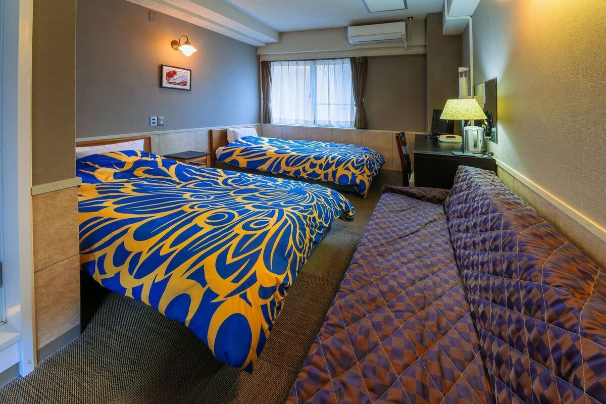 A hotel room with two beds, a desk, a lamp, and an air conditioning unit.