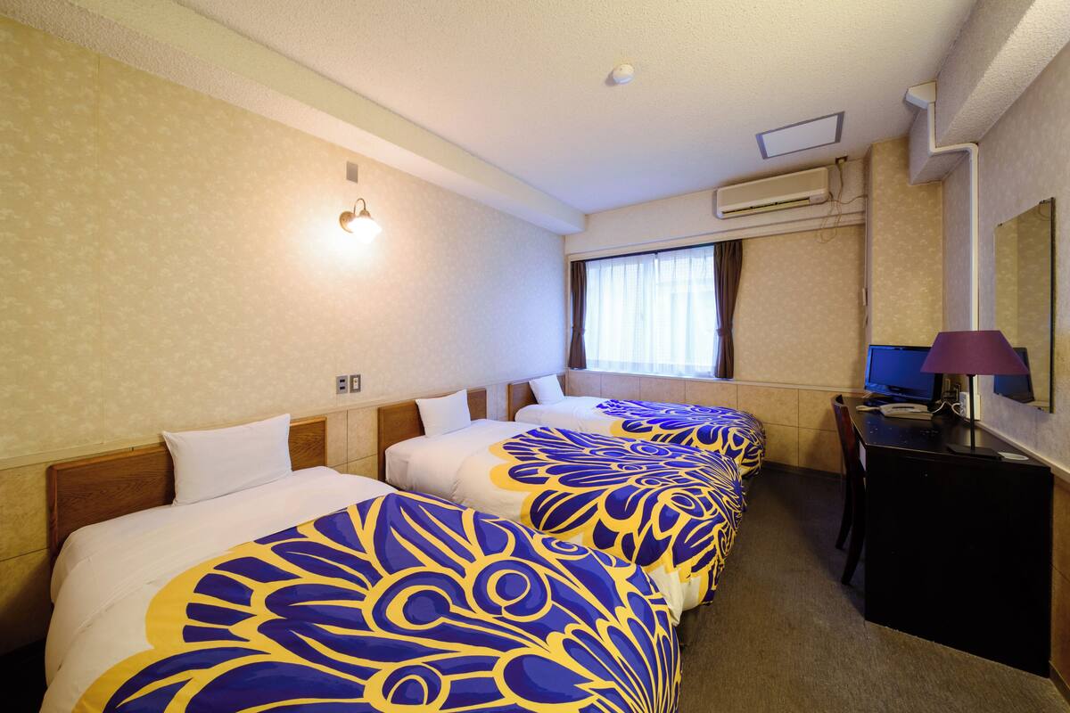 A hotel room with two beds, a desk, a chair, a lamp, and a window with curtains.