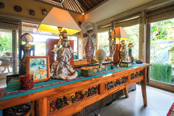 Une pièce dotée d’une table en bois où sont exposés divers objets d’art et d’artisanat, d’une grande fenêtre donnant sur un paysage verdoyant et d’un plafond au décor traditionnel.
