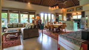 A spacious living area with a high ceiling, large windows, and a dining area with a kitchen in the background. - Gorgeous, 3-bedroom Villa in the village of Penestanan/Ubud with AC, WiFi, Pool. (Bali)