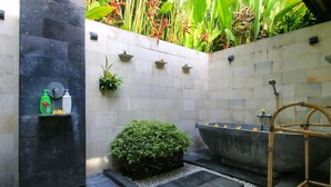 A modern bathroom with a freestanding bathtub, a small shelf with toiletries, and a potted plant. - Gorgeous, 3-bedroom Villa in the village of Penestanan/Ubud with AC, WiFi, Pool. (Bali)