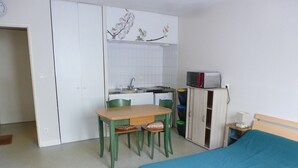 A compact room with a bed, a small table with chairs, a kitchenette, and a wardrobe. - Appartement Plain-pied Proche Thermes Parking Privée (Bagnères-de-Bigorre)