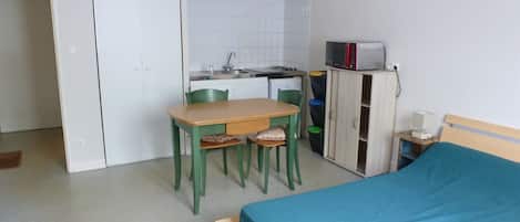 A compact room with a bed, a small table with chairs, a kitchenette, and a wardrobe.