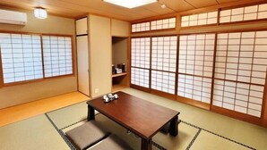 Une pièce de style japonais traditionnel, avec un sol recouvert de tatamis, des portes coulissantes, une table en bois et un luminaire suspendu au plafond.