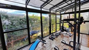 Une salle de sport équipée de matériel d’exercice et dotée de grandes fenêtres donnant sur un jardin.