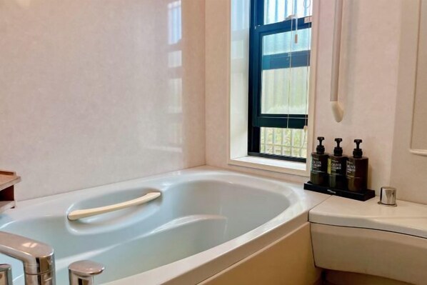 A bathroom with a bathtub, a window, and toiletries on the counter. - Vacation Rental Hanatsusuri Izukogen (Ito)