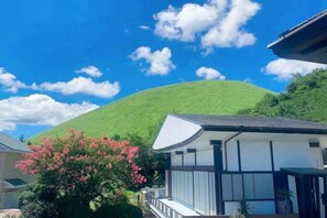 A modern building with a flat roof and large windows, surrounded by greenery and a hill in the background. - Vacation Rental Hanatsusuri Izukogen (Ito)