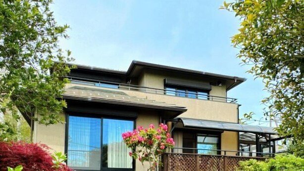 Un bâtiment moderne à deux étages, doté d’un balcon et d’un jardin agrémenté de diverses plantes et fleurs.