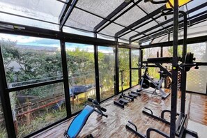 Un gimnasio con equipo de ejercicio y grandes ventanales con vistas a un paisaje natural.