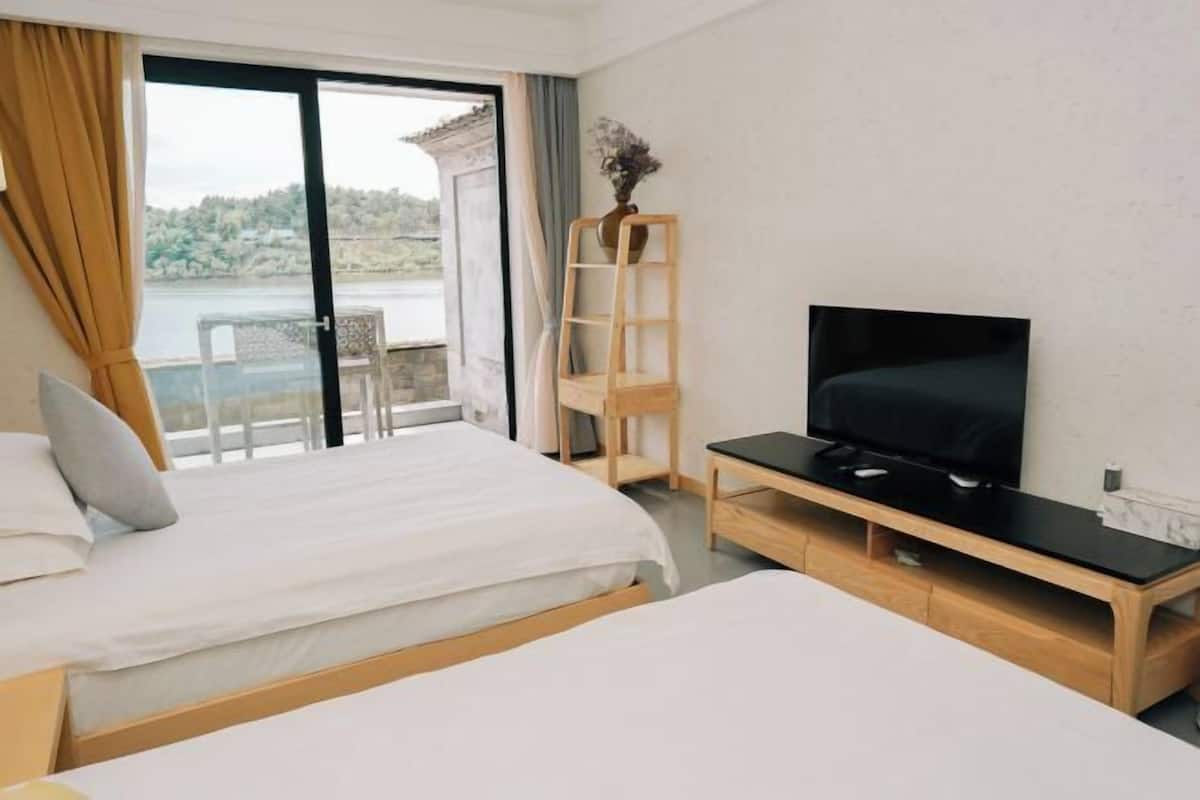 A hotel room with two beds, a TV, a wooden shelf, and a view of a body of water.