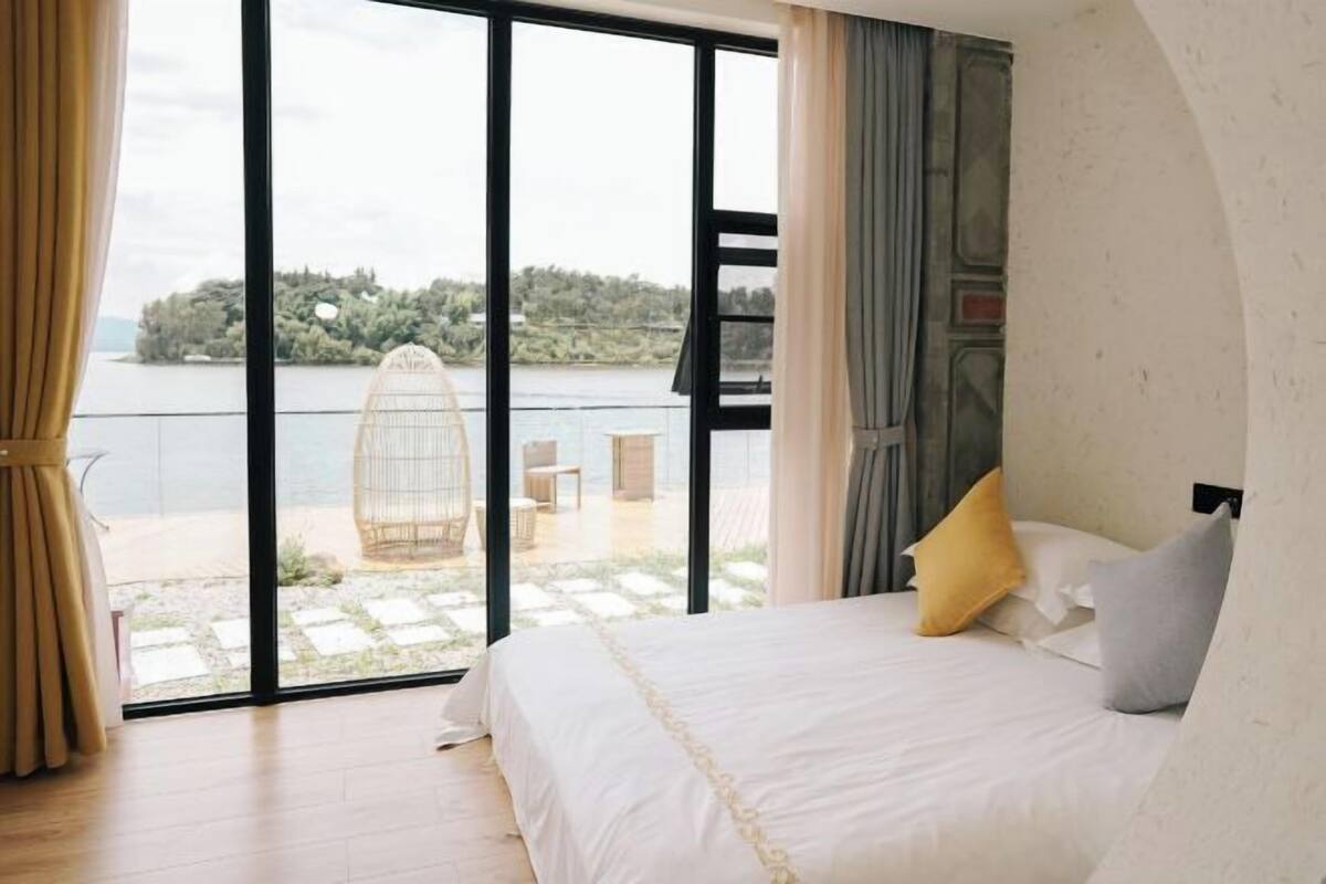 A bedroom with a large window, a bed, and a view of a body of water.