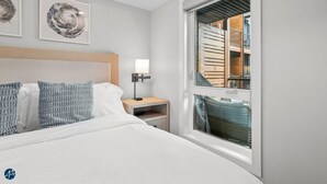 A hotel room with a bed, bedside table, lamp, and a window with a view of a building. - 1 Bed/1 Bath Sparrowhawk-Courtyard Facing-Sleeps 4 (Dead Man's Flats)